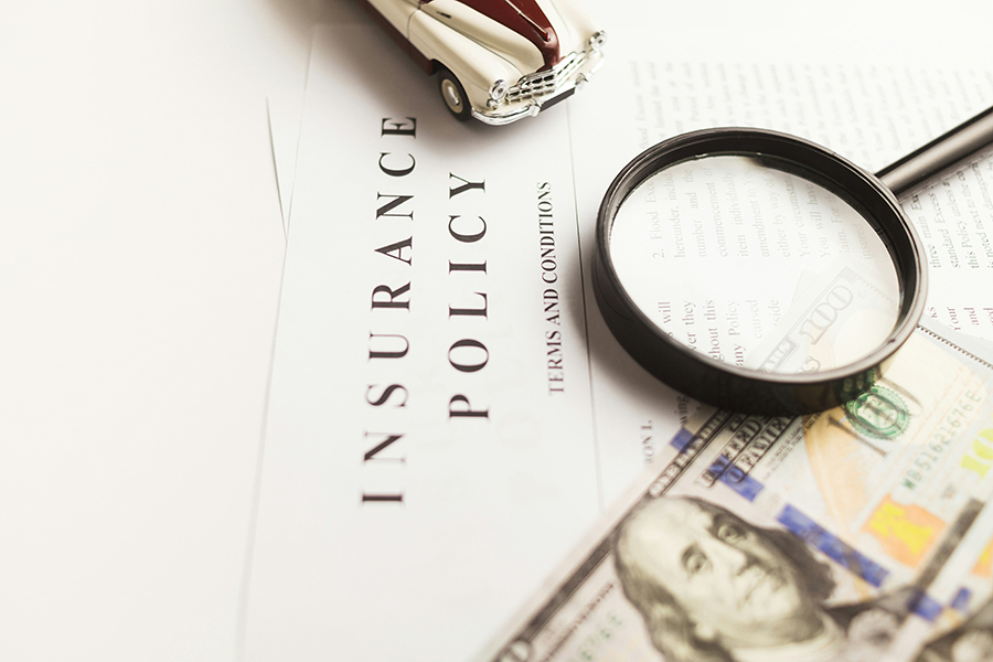 Home insurance policy document on a desk with money and a magnifying glass, symbolizing the cost and details of homeowners insurance in Marquette, MI.